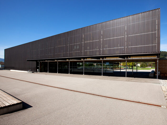 Mittelschule mit Profilfassade aus Kuper. Metallfassade im Fassadensystem P2 Trapezprofil / Trapezblech mit Perforation. Kupferfassade kombiniert mit Holzfassade.